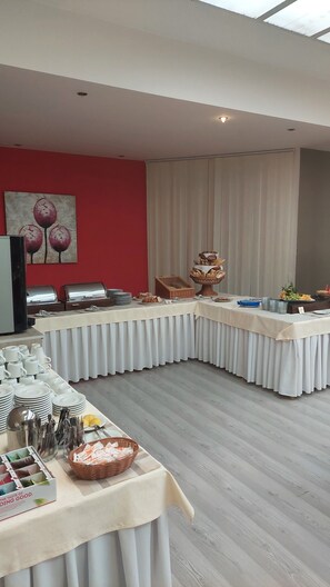 A buffet setup with various food items and utensils, a red wall with a floral painting, and a ceiling with natural light. - Hotel Belaria Resort (Hradec nad Moravicí)