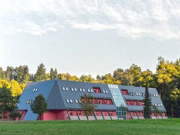 A multi-story building with a sloped roof, red and blue exterior walls, and multiple windows. - Hotel Belaria Resort (Hradec nad Moravicí)