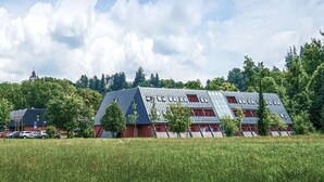 Um edifício moderno com um design de telhado singular, rodeado por um campo verde e árvores.