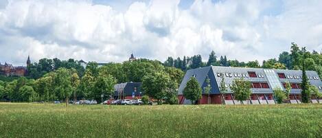 A modern building with a unique roof design, surrounded by a green field and trees.