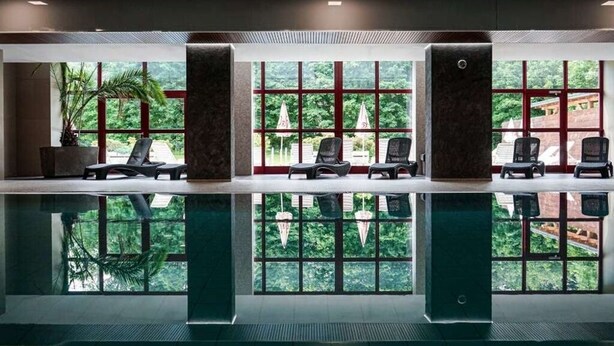 Área da piscina com espreguiçadeiras e amplas janelas com vista para o verde.