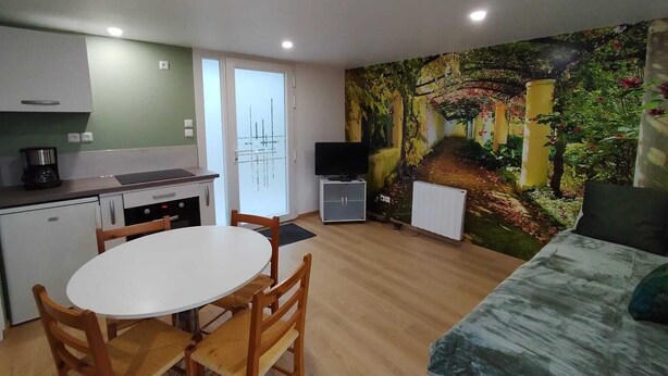 A compact living space with a kitchenette, a dining area, a flat-screen TV, and a mural of a garden scene. - Maisonnette à la Campagne " le Grain de Sel" (Hampont)