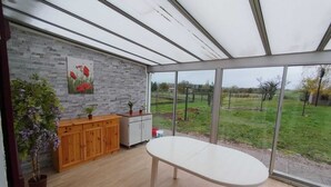 A conservatory with a wooden cabinet, a white table, and a view of a green landscape. - Maisonnette à la Campagne " le Grain de Sel" (Hampont)