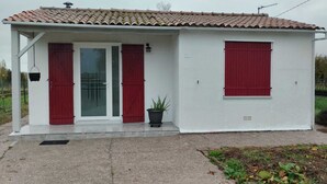 A small, single-story building with a tiled roof, white exterior walls, and red shutters on the doors and windows. - Maisonnette à la Campagne " le Grain de Sel" (Hampont)