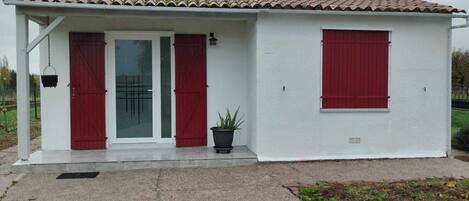 A small, single-story building with a tiled roof, white exterior walls, and red shutters on the doors and windows.