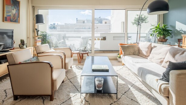 Ein modernes Wohnzimmer mit einer Couch, Sesseln, einem Couchtisch und einem Fernseher.
