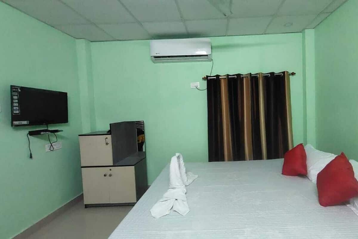 A hotel room with a bed, a TV, a desk, and an air conditioner.