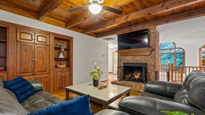Un salón acogedor con sofás de cuero, chimenea, armarios de madera y ventilador de techo.