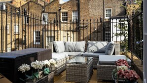 Un espace patio aménagé avec des meubles en osier, une table à plateau en verre et des plantes en pot.