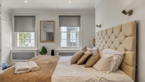 Une chambre avec un grand lit, deux fenêtres équipées de stores, un miroir et un radiateur.