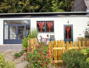 Una casa moderna con un amplio ventanal, dos ventanas con cortinas rojas y una cerca de madera.