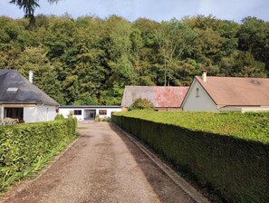 A pathway leading to a modern house with a sloped roof, surrounded by dense greenery and a well-maintained hedge. - L'orée du Bois (Daubeuf-Serville)