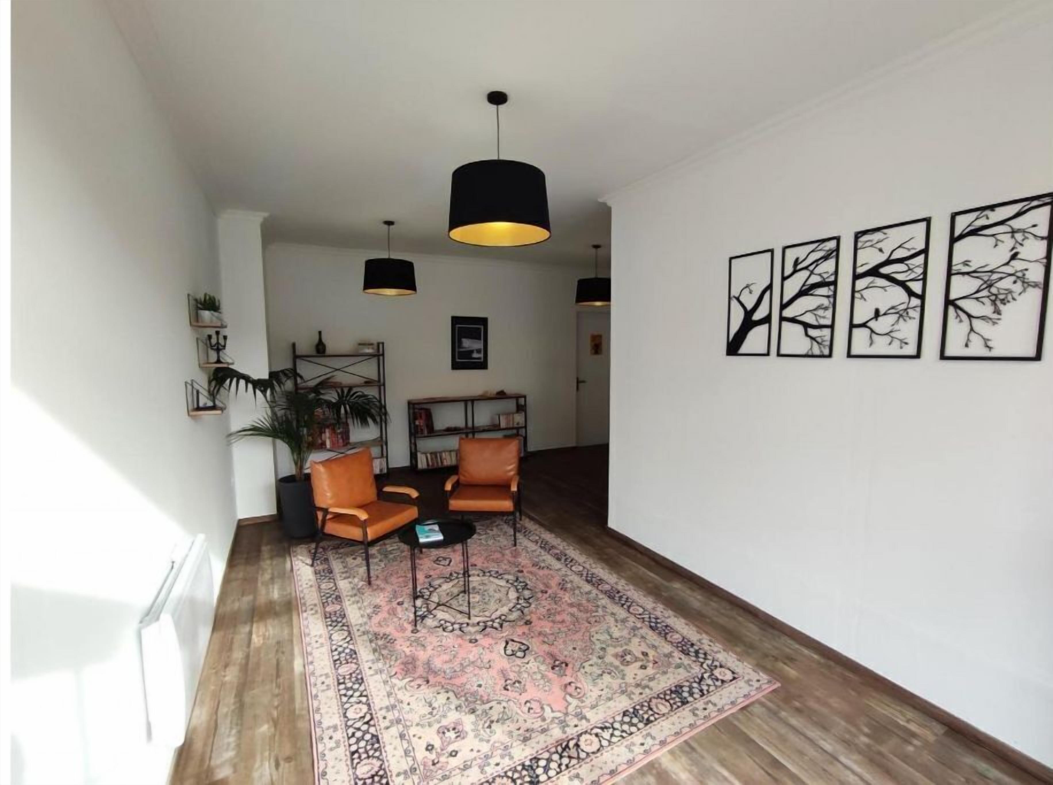 A living room with a large rug, two leather chairs, a bookshelf, and three wall-mounted artworks.