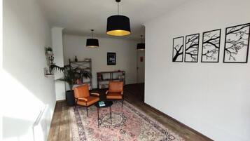 A living room with a large rug, two leather chairs, a bookshelf, and three wall-mounted artworks.