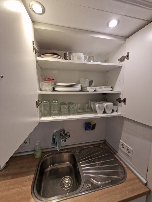 A compact kitchen with white cabinets, a stainless steel sink, and a dish rack.