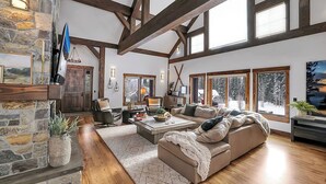 Un salón amplio con chimenea de piedra, ventanas grandes y un techo alto con vigas a la vista.