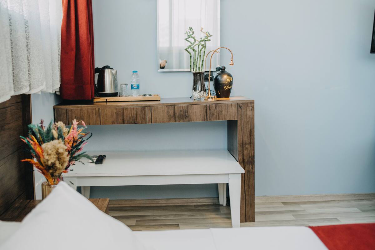 A hotel room with a bed, a wooden console table with a vase of flowers, a coffee maker, and a framed picture on the wall.