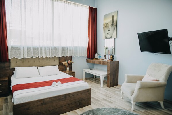 A bedroom with a bed, a desk, a chair, a TV, and a window with curtains. - MYMAHALL HOTEL (Izmir)