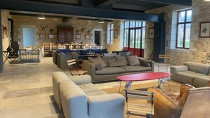 A spacious living area with a stone wall, a dining area with a kitchen in the background, and large windows providing natural light. - La Domaine de Grandmont Evenements (Bonneuil-Matours)