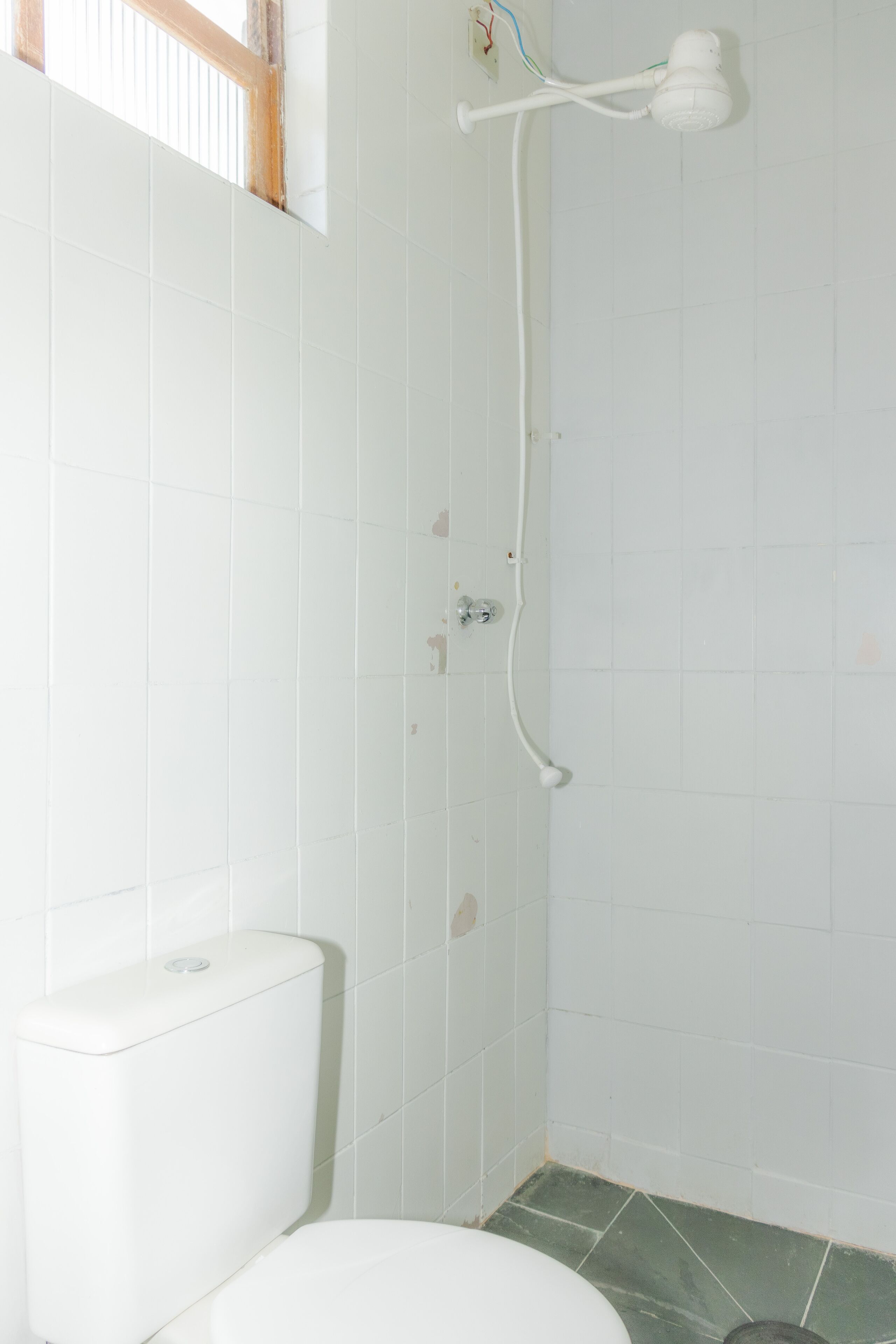Un baño con inodoro, ducha con cabezal de ducha manual y ventana.