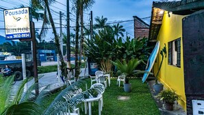 A courtyard with outdoor seating, palm trees, and a yellow building. - Pousada Chalé do Beija-flor  (Ubatuba)