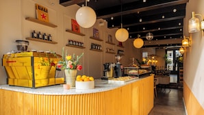 A reception area with a wooden counter, shelves with jars, a coffee machine, and a view into the dining area. - This hotel is a 1 bedroom(s), 1 bathrooms, located in Delft, Zuid-Holland. (Delft)