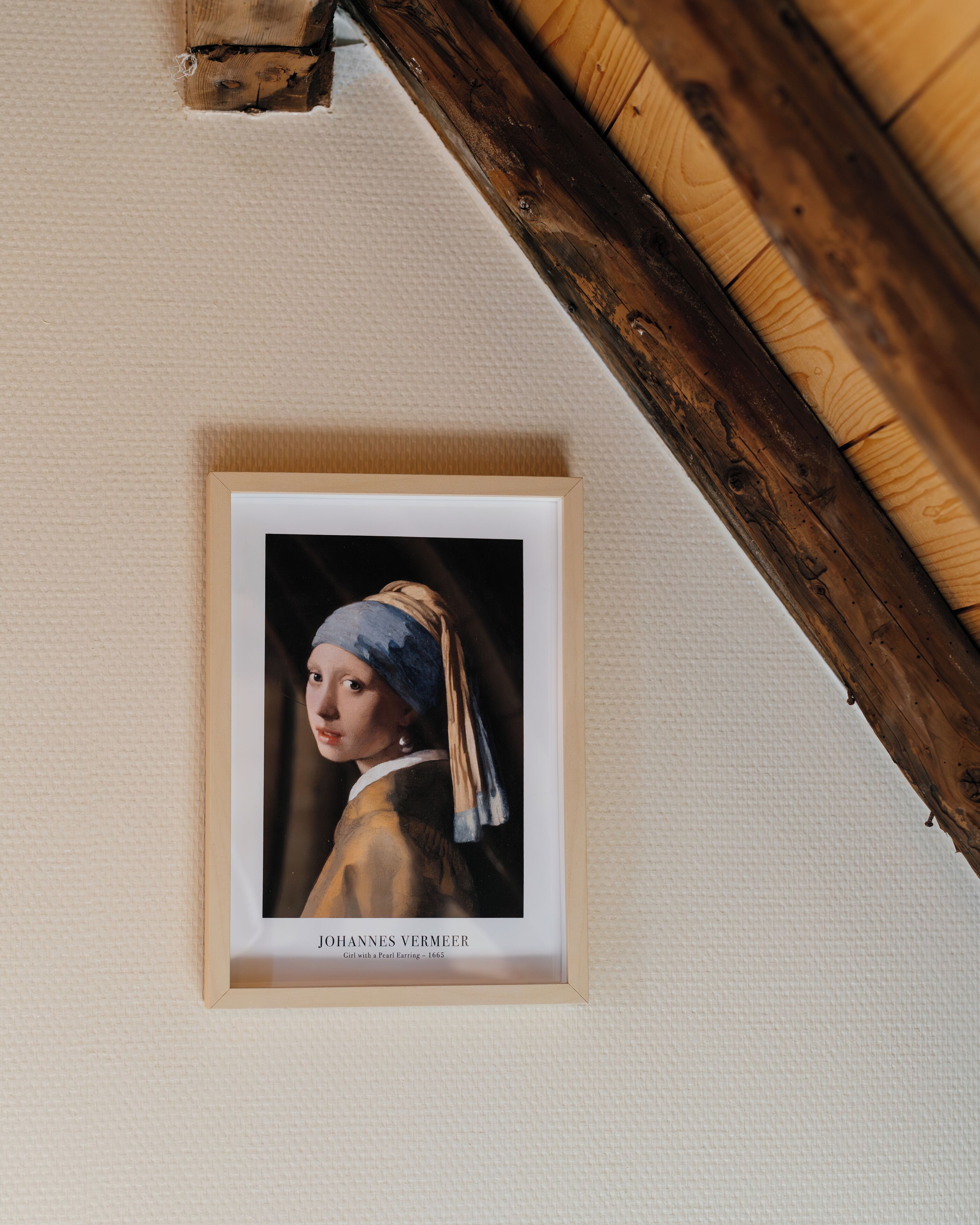 Een lijstwerk met het kunstwerk 'Het meisje met de parelketting' van Johannes Vermeer op een gestructureerde muur.