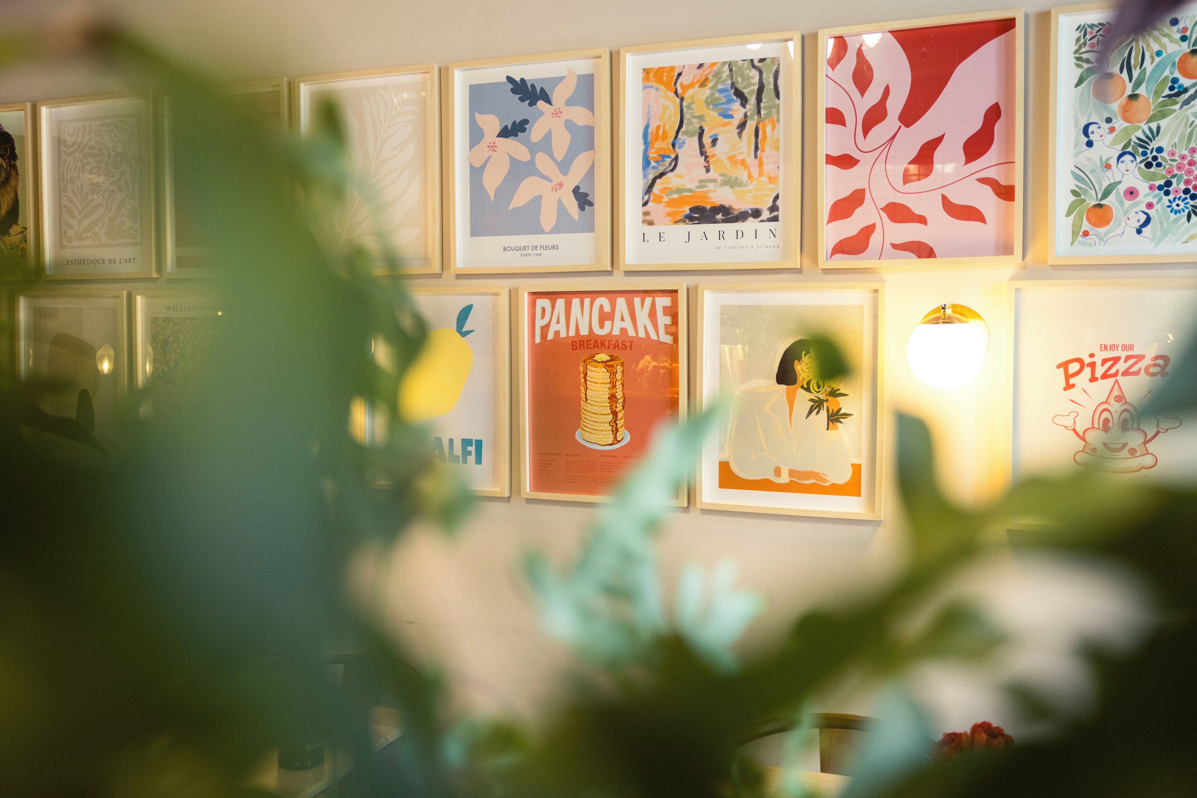 A wall with various framed artworks, including a 'Pancake Breakfast' poster and a 'Pizza' sign.
