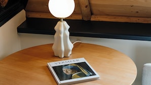 A round wooden table with a white lamp and a book titled "VERMEER" on it. - This hotel is a 1 bedroom(s), 1 bathrooms, located in Delft, Zuid-Holland. (Delft)