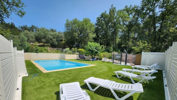 Un jardin avec une piscine, de l’herbe artificielle verte et des chaises longues blanches.
