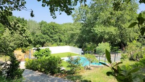 Un jardin à l’arrière de la maison, avec une piscine, entouré d’arbres et délimité par une clôture blanche.