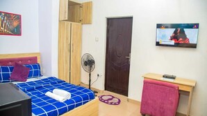 Ein Schlafzimmer mit Bett, Fernseher, Holzschrank, Ventilator und Schreibtisch.