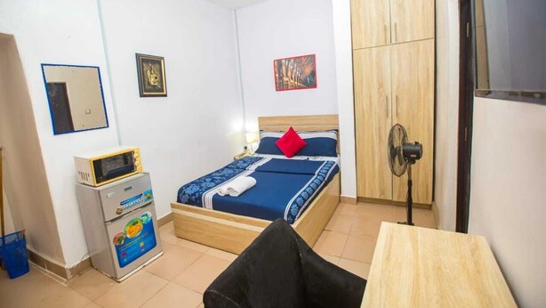 Ein Schlafzimmer mit einem Bett, einem Nachttisch, einem Ventilator, einer Mikrowelle und einem Schrank.