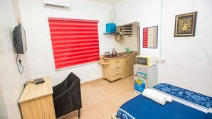 Ein Schlafzimmer mit einem Bett, einem Schreibtisch, einem Stuhl, einem Kleiderschrank, einem Fenster mit Jalousien, einem Spiegel und einer Klimaanlage.