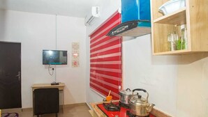 Eine kompakte Küche mit Gasherd, Wasserkocher und Mikrowelle. Über dem Herd befindet sich ein kleines Holzschränkchen und an der Wand ist ein Fernseher angebracht.