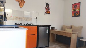 Kompakti keittiö, jossa on jääkaappi, liesi ja oranssit kaapit. Keittiössä on puinen pöytä, jossa on tuoli, sekä pieni sivupöytä.
