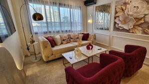 Ein Wohnzimmer mit einem beigen Sofa, roten Sesseln, einem weißen Couchtisch und einer großen Wanddekoration mit floralem Muster.