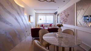 Ein modernes Wohnzimmer mit einem runden Marmortisch, beigen Sesseln, einem roten Sofa und einer Wand mit einem floralen Wandbild.
