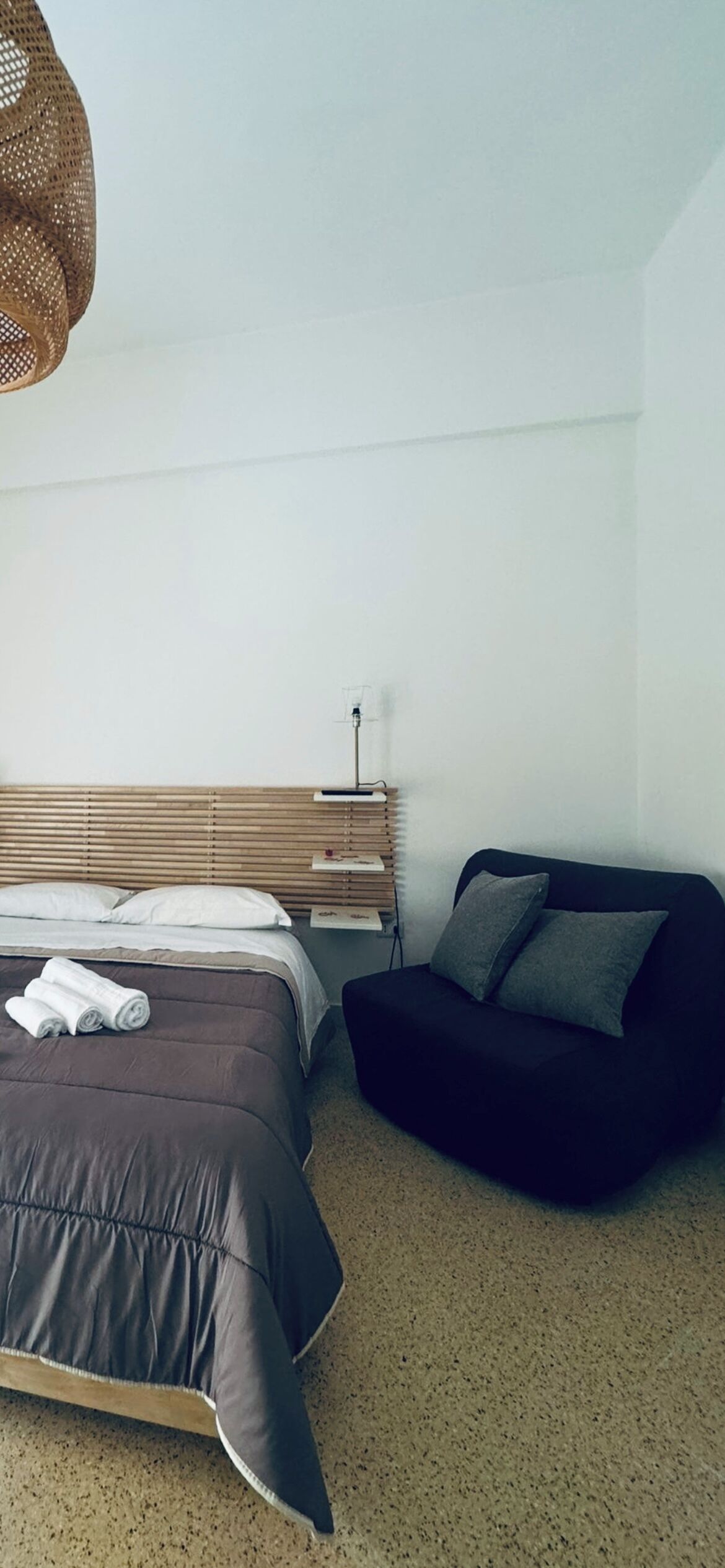 Una camera da letto con un letto, un divano nero, una testiera in legno e una lampada a sospensione.