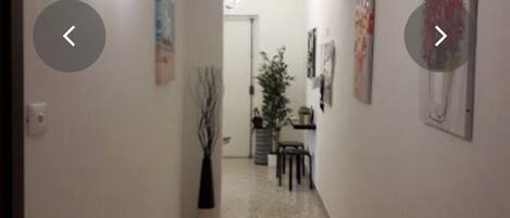 A hallway with a tiled floor, a potted plant, and artwork on the walls.