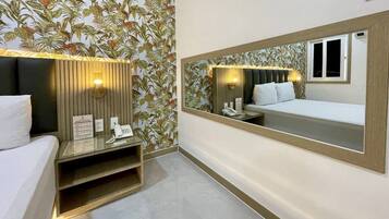 A hotel room with a bed, bedside table, and a large mirror reflecting the room.