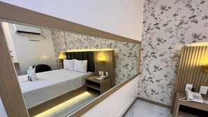 Una habitación de hotel con cama, mesita de noche y un espejo grande.