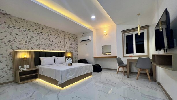 Habitación de hotel moderna con cama, mesita de noche, lámpara, escritorio, sillas y televisión.