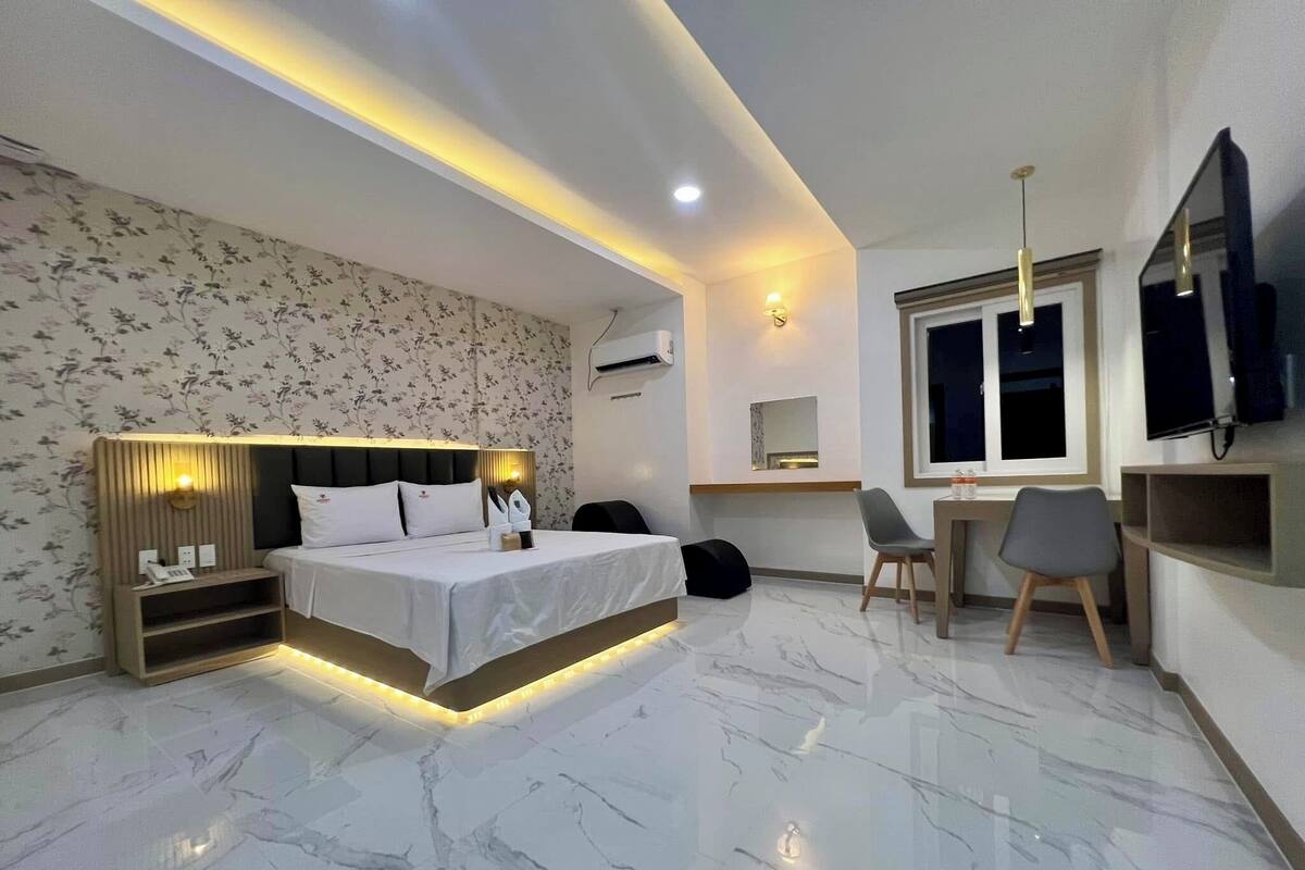Une chambre d’hôtel moderne équipée d’un lit, d’une table de chevet, d’une lampe, d’un bureau, de chaises et d’un téléviseur.