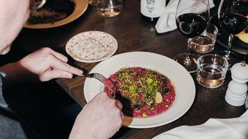 Una persona cenando en una mesa con un plato de comida, una botella de vino y copas.