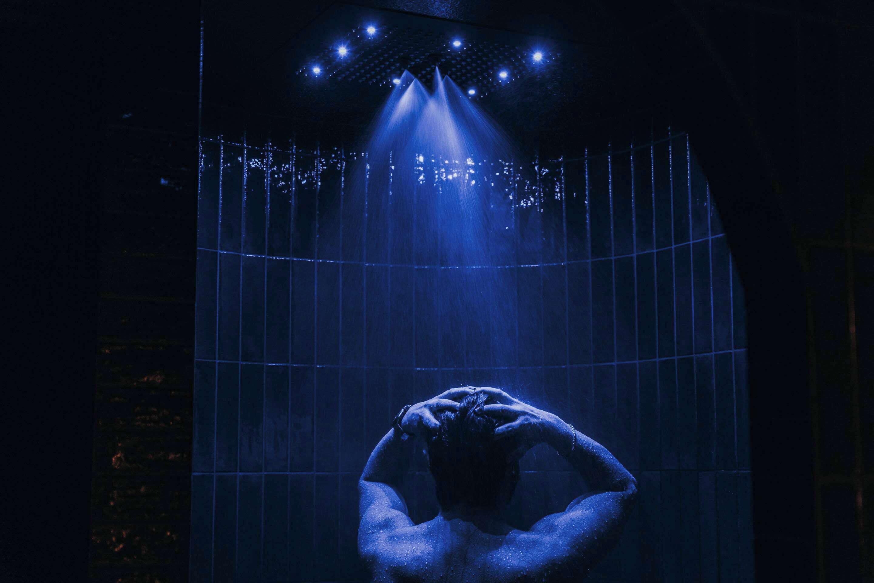A person in a shower with blue lighting and water jets.