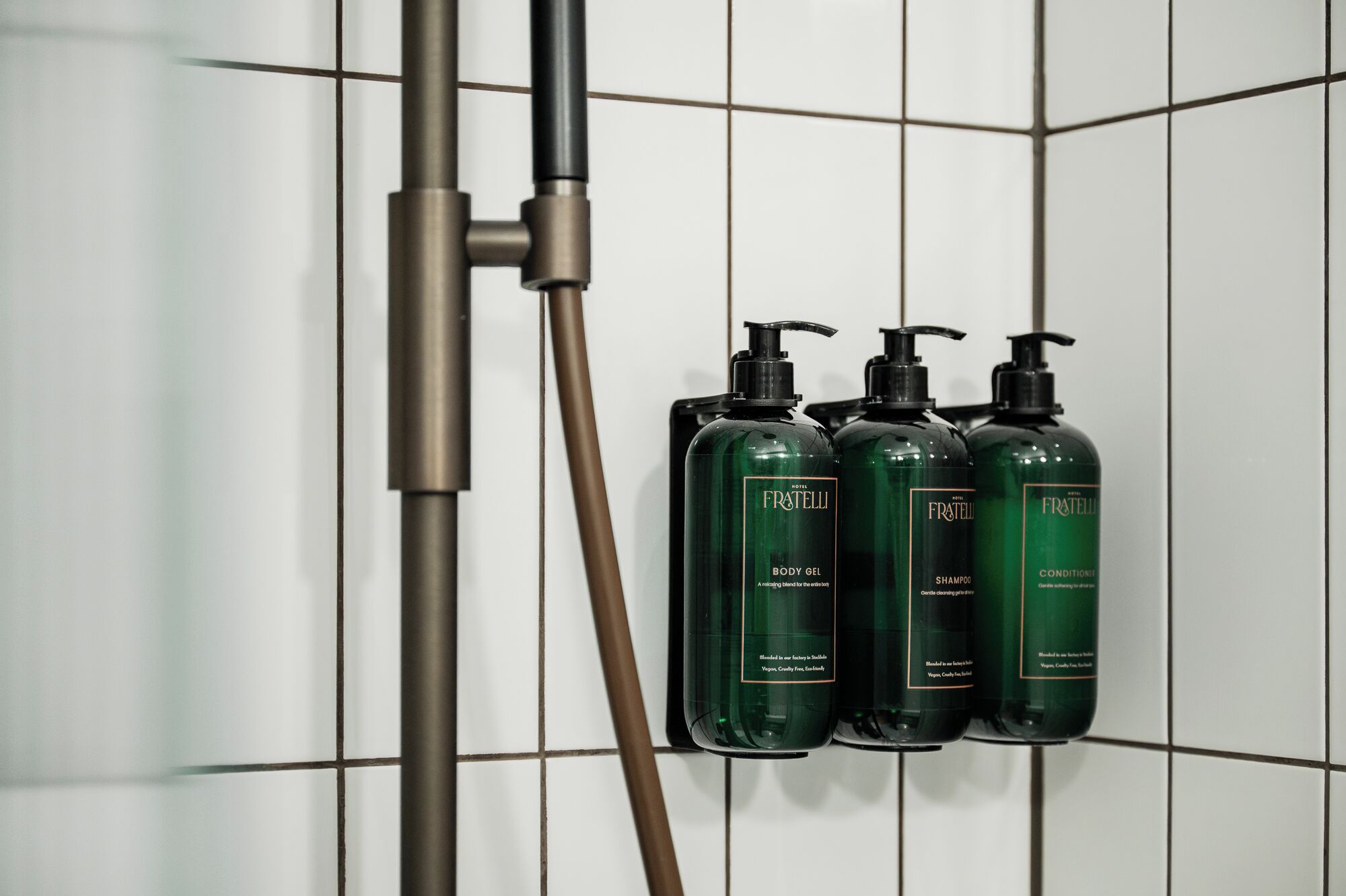 Baño con ducha y tres botellas verdes de productos Fratelli.
