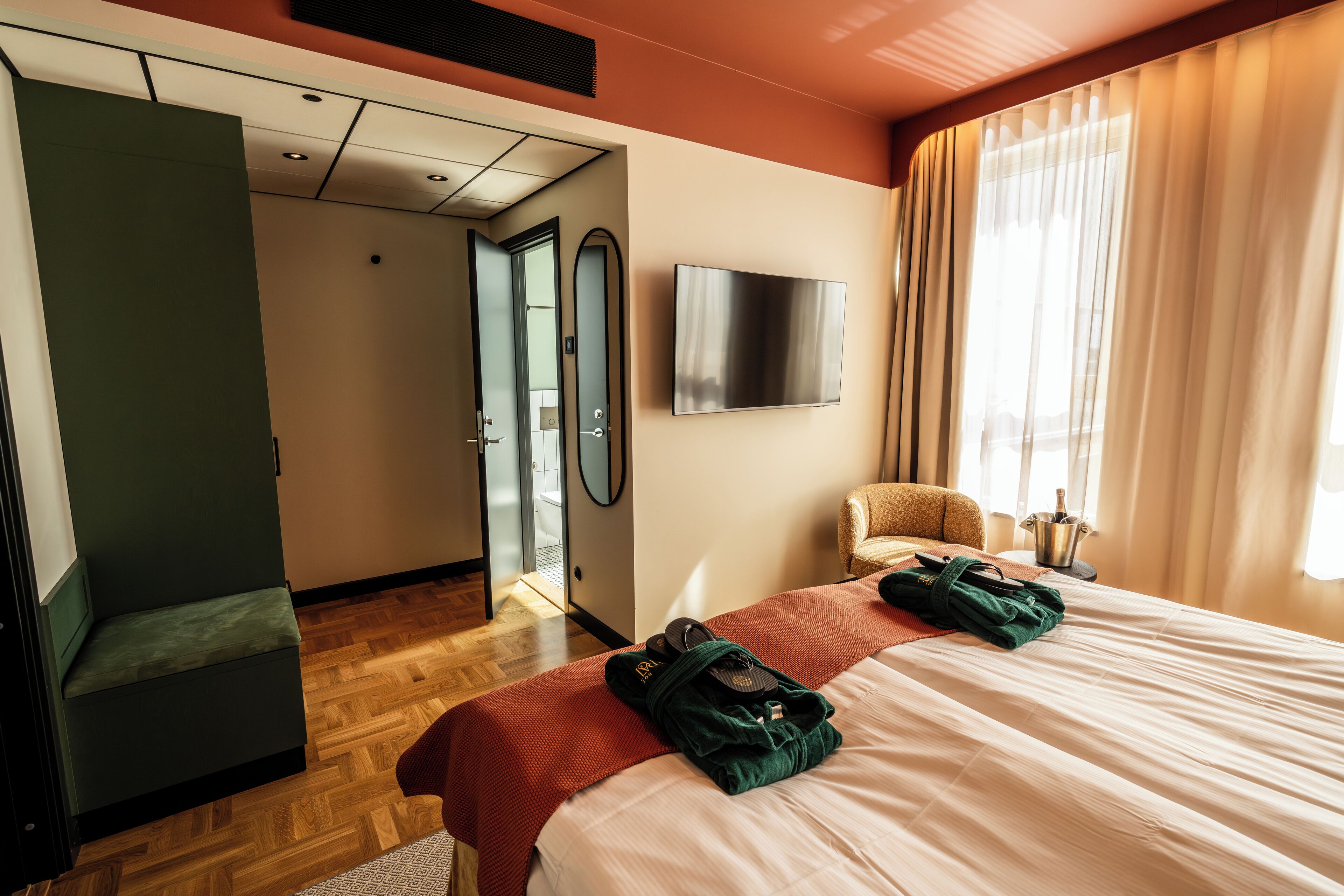 Una habitación de hotel con una cama, una silla, un televisor y un espejo.