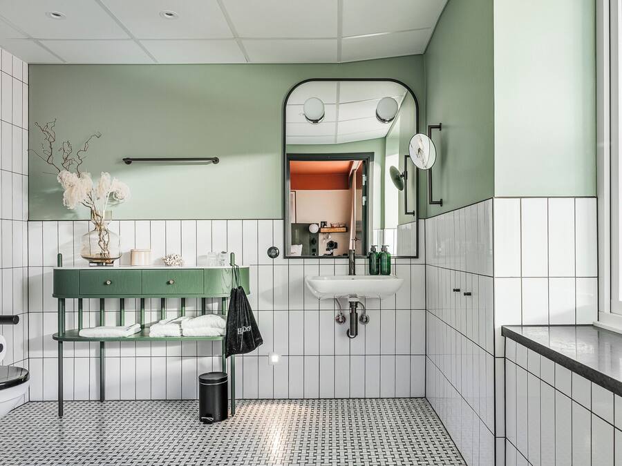 A bathroom with a green vanity, white tiles, a sink, and a mirror.
