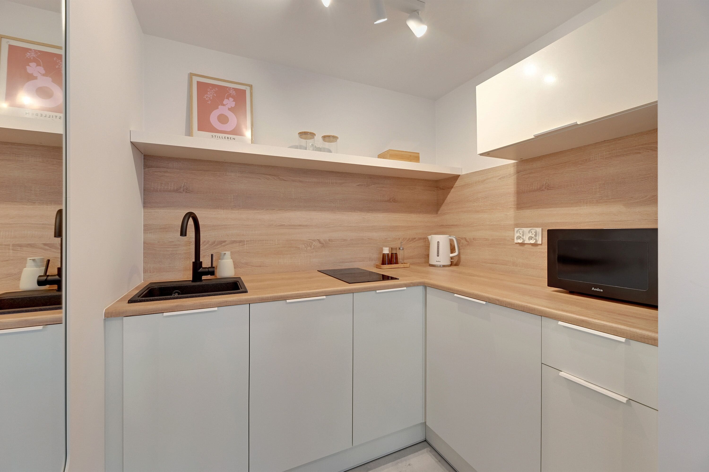 Une cuisine moderne avec des meubles blancs, un plan de travail en bois, un robinet noir, une bouilloire et un four à micro-ondes.